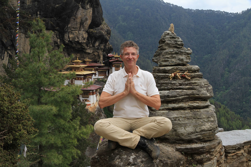 Martin sitzt auf einem Stein, die Hände gefaltet, im Hintergrund ein fernöstliches Kloster